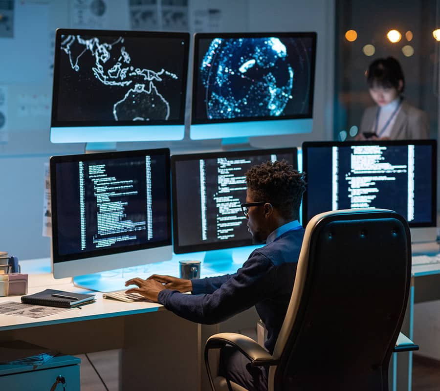 IT-Sicherheitscheck: Webseiten Bild mit Mann sitzend am Schreibtisch vor fünf Monitoren. Er ist IT-Security Spezialist.
